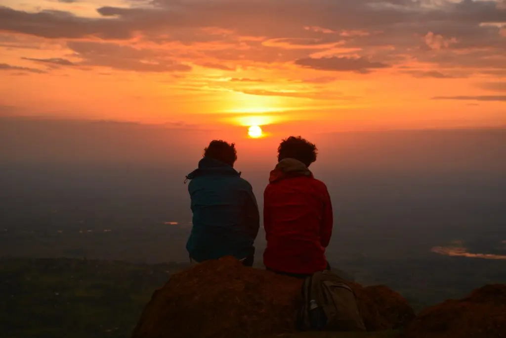 Two travelers sitting together watching the sunset over Sipi Falls,overlooking the flat plains below the horizons of Karamoja-Teso region near lake Bisina and Lake Opeta