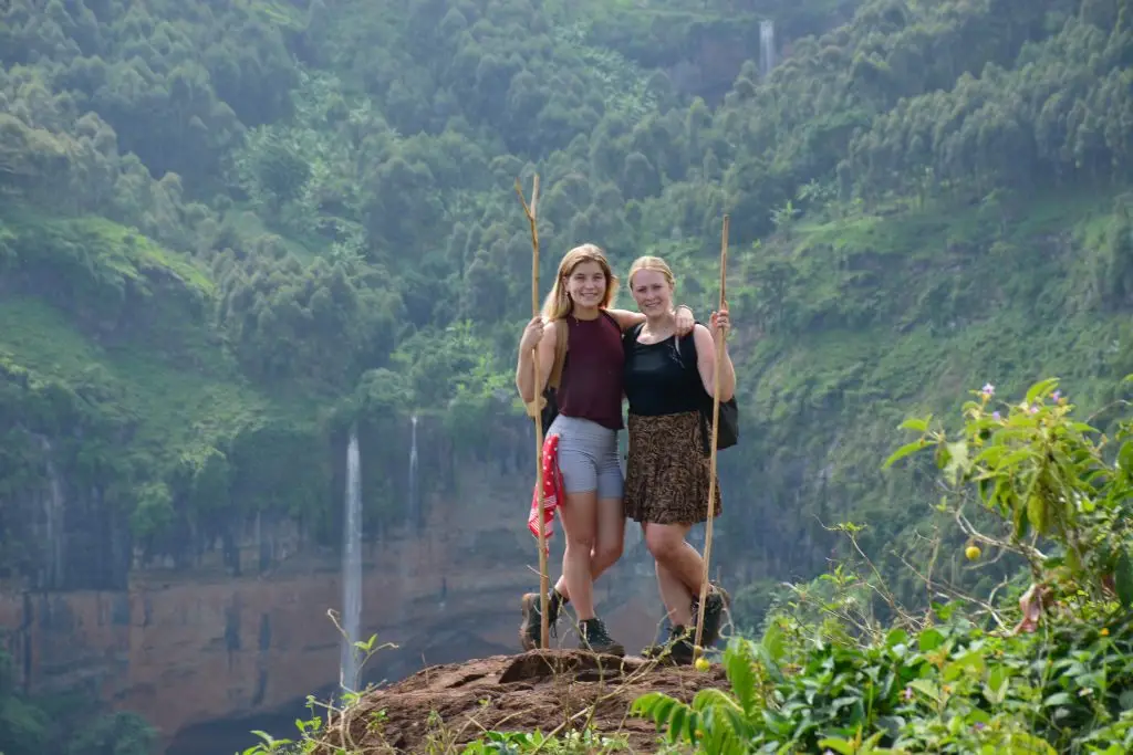 Hikers standing on a viewpoint overlooking Chebonet Waterfalls and the green slopes of Mount Elgon Uganda