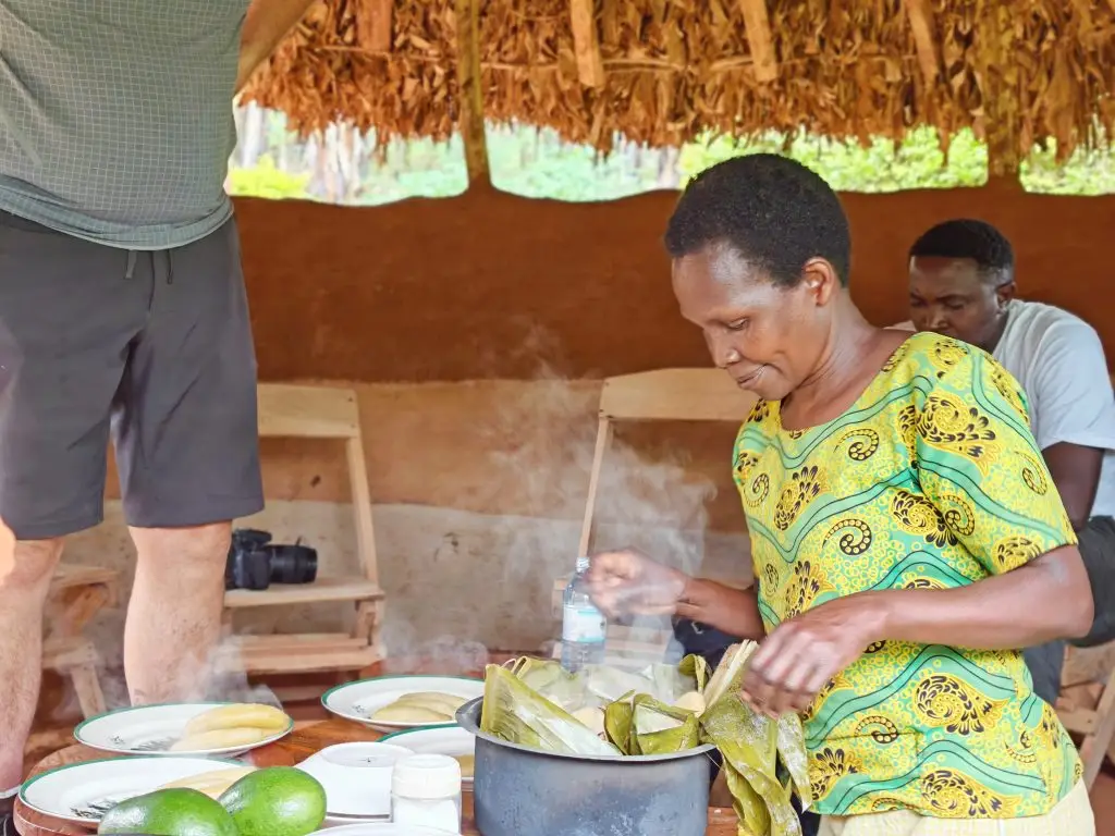 Local Woman serving traditional food in banana leaves during the Sipi Local Cooking Experience in Sipi Falls, Uganda.