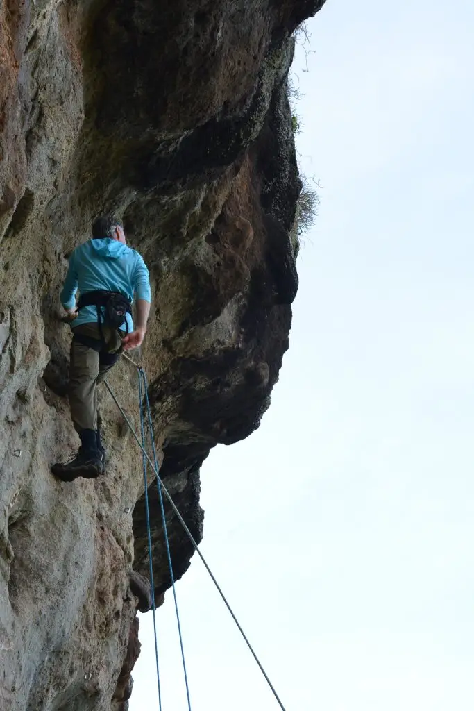 Guided Sipi Rock Climbing experience in Uganda Rock Climber ascending on the volcanic cliffs near Sipi Falls in Eastern Uganda with safety ropes and views along the valley and the flat plains